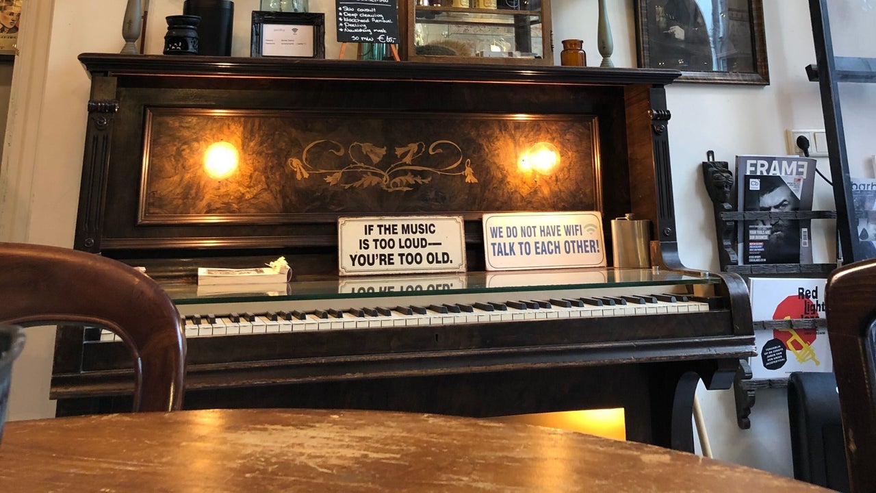 Een oude zwarte piano in de salon met twee bordjes: If the music is too loud, you're too old, en We do not have wifi, talk to each other